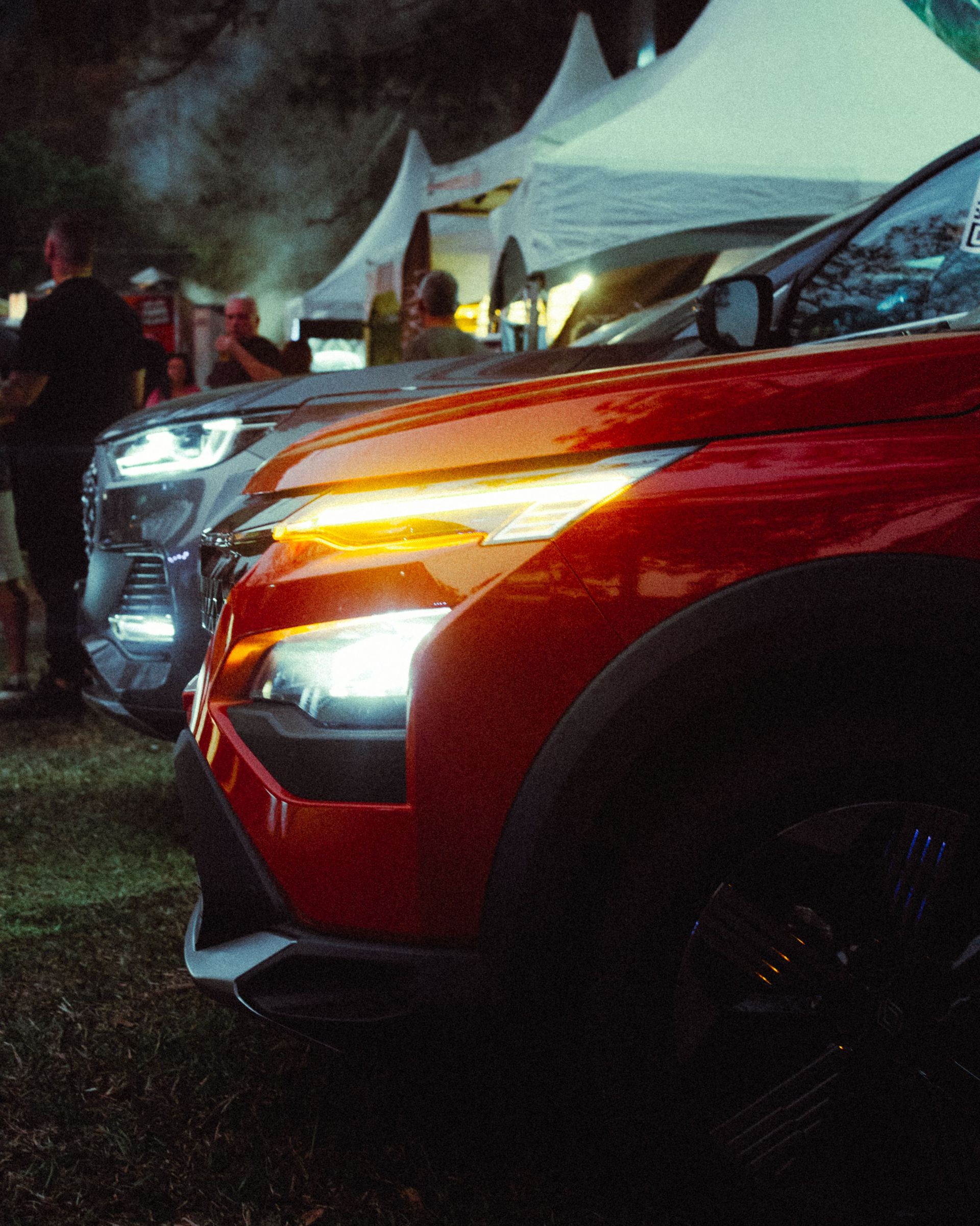 Close-up of a red car with its headlights on at a night car exhibition, showcasing automotive beauty.
